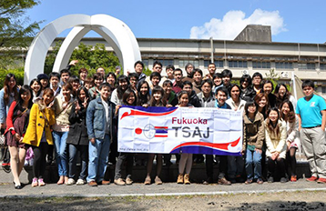 Group photo of students gathered outdoors on a sunny day, holding a banner with the words &quot;Fukuoka TSAJ&quot;.