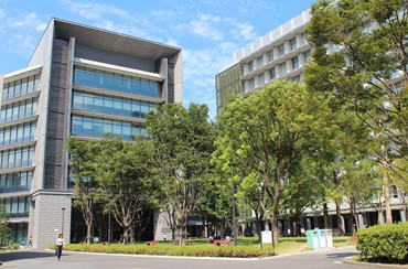 福冈大学的建筑物外观。建筑物前方有数棵高大的树木耸立着。